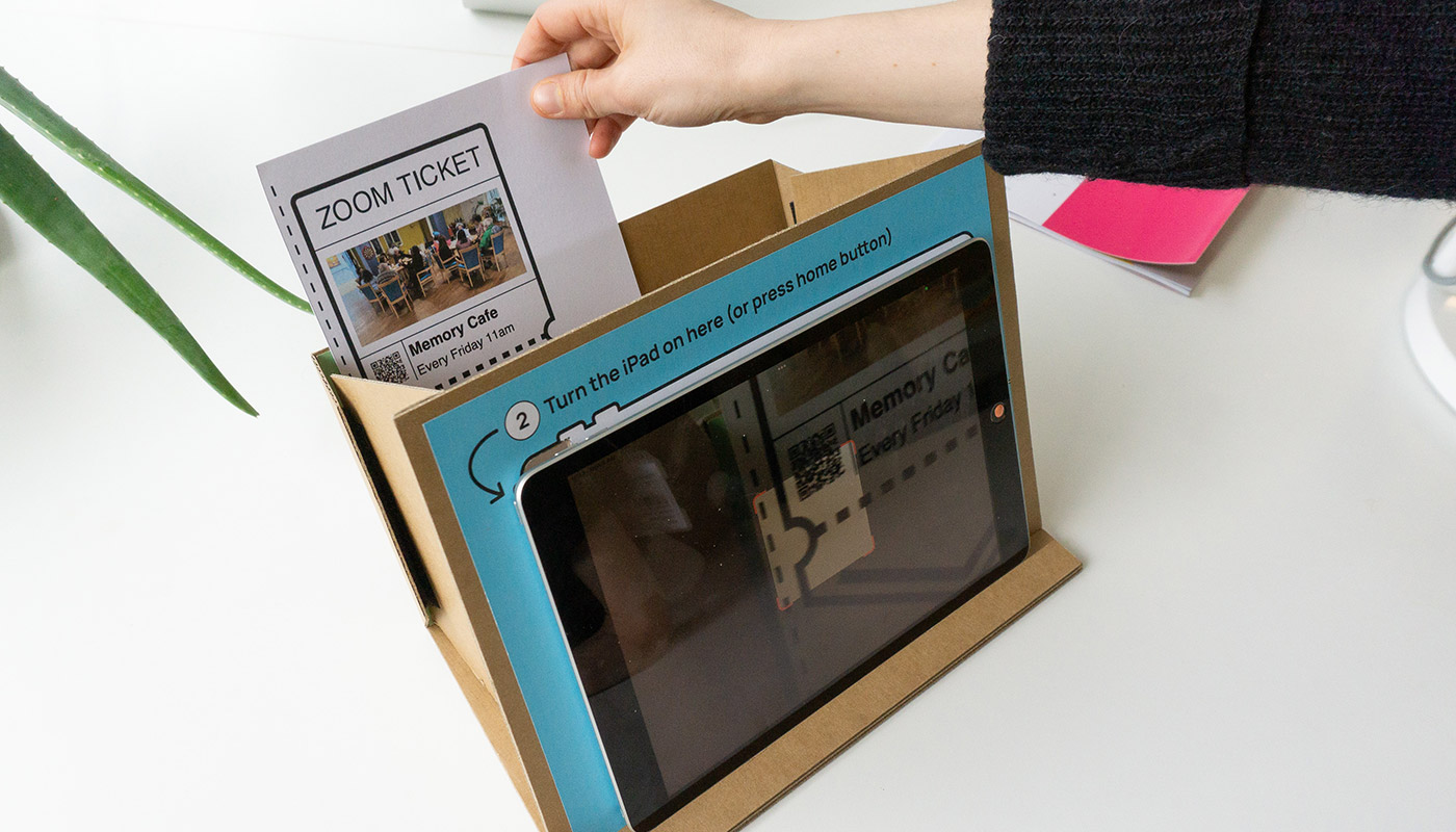 A laptop on a carboard stand with printed Zoom meeting invite